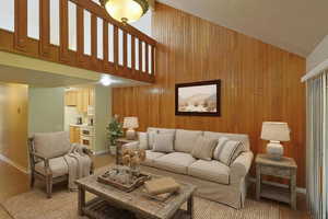 Virtually staged living area with wood walls, high vaulted ceiling, light wood-style flooring, an accent wall, and a textured ceiling