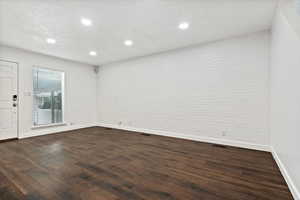 Spare room featuring dark wood finished floors, recessed lighting, and brick wall