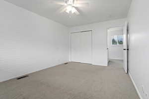 Unfurnished bedroom with carpet floors, ceiling fan, a closet, and brick wall