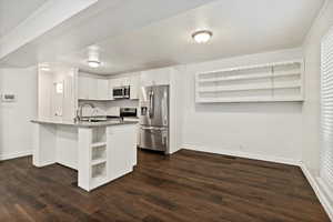 Kitchen with open shelves, white cabinets, appliances with stainless steel finishes, dark wood-style flooring, and ornamental molding