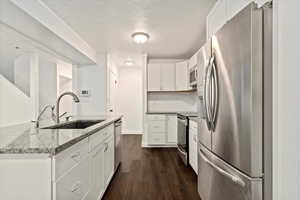 Kitchen with stainless steel appliances, a textured ceiling, dark wood-type flooring, white cabinets, and light stone counters