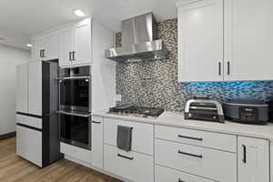Kitchen with white cabinetry, wall chimney exhaust hood, decorative backsplash, stainless steel appliances, and dark wood-style flooring