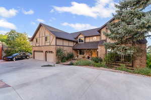 English style home with driveway, a garage, brick siding, and stucco siding