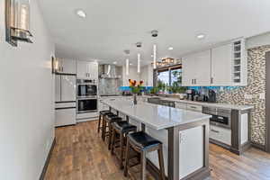 Kitchen featuring a breakfast bar area, light stone counters, pendant lighting, dark wood-style flooring, and recessed lighting