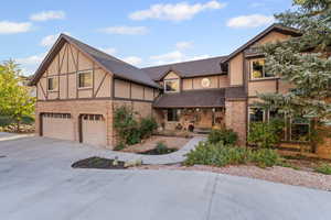English style home with stucco siding, a porch, a garage, concrete driveway, and a shingled roof