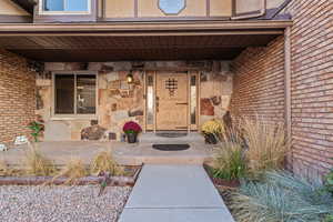 Entrance to property featuring stone siding, brick siding, and covered porch