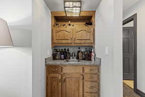 Indoor wet bar featuring brown cabinets, wood finished floors, and light stone counters