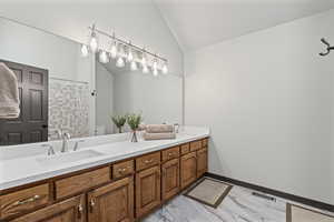 Bathroom with double vanity, a tile shower, vaulted ceiling, and light marble finish flooring