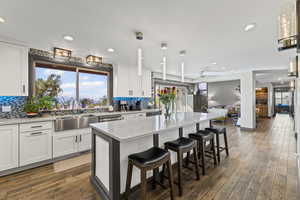 Kitchen with white cabinetry, a kitchen bar, decorative backsplash, dark wood-style flooring, and recessed lighting