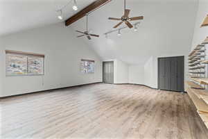 Unfurnished living room with track lighting, light wood finished floors, high vaulted ceiling, beam ceiling, and ceiling fan