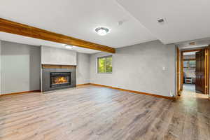 Unfurnished living room with beam ceiling, light wood-style floors, a tiled fireplace, and heating unit