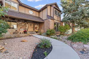 View of front of house featuring stucco siding, a shingled roof, and stone siding