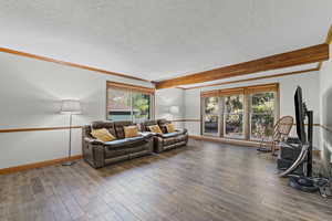 Living area featuring beamed ceiling, a textured ceiling, wood-type flooring, and crown molding