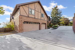 View of side of home featuring brick siding, an attached garage, stucco siding, and driveway