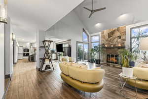 Living room featuring ceiling fan, high vaulted ceiling, wood-type flooring, and a fireplace