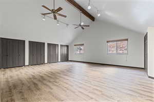 Unfurnished bedroom with rail lighting, two closets, high vaulted ceiling, light wood finished floors, and beamed ceiling