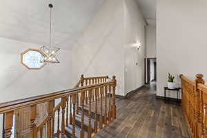 Hallway featuring an upstairs landing, high vaulted ceiling, dark wood-style flooring, and a chandelier