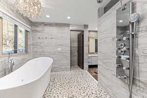 Full bathroom featuring tile walls, a soaking tub, vanity, a chandelier, and a shower