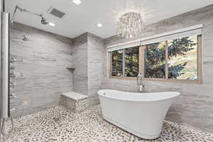 Bathroom featuring tile walls, a soaking tub, a chandelier, and tiled shower
