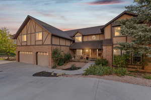 Tudor home featuring stucco siding, an attached garage, concrete driveway, and brick siding