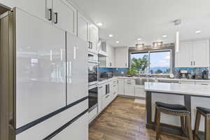 Kitchen with white fridge, white cabinetry, pendant lighting, light stone countertops, and tasteful backsplash