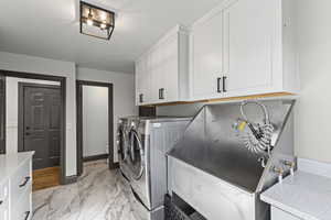 Washroom with light marble finish flooring, washer and clothes dryer, and cabinet space. Full dog bath station