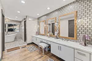 Full bathroom with double vanity, a soaking tub, light wood finished floors, and recessed lighting