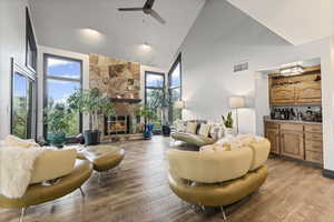Living area featuring high vaulted ceiling, plenty of natural light, light wood-style floors, ceiling fan, and a fireplace