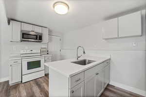 Kitchen with electric stove, stainless steel microwave, a peninsula, dark wood-style floors, and white cabinetry