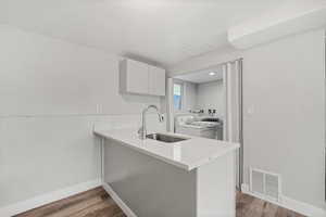 Kitchen featuring a peninsula, white cabinetry, light wood finished floors, washing machine and clothes dryer, and light stone countertops