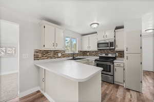 Kitchen with light countertops, appliances with stainless steel finishes, a peninsula, decorative backsplash, and a textured ceiling