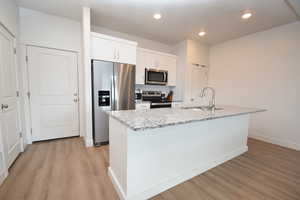 Kitchen with appliances with stainless steel finishes, light stone counters, decorative backsplash, white cabinetry, and light wood-style flooring