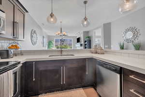 Kitchen featuring stainless steel appliances, a chandelier, decorative light fixtures, dark brown cabinetry, and light stone countertops