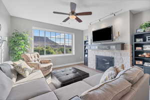 Living room with track lighting, a fireplace, a ceiling fan, and wood finished floors