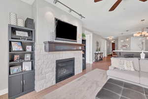 Living area featuring a ceiling fan, rail lighting, a fireplace, a chandelier, and light wood finished floors