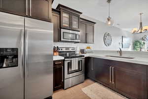 Kitchen featuring stainless steel appliances, pendant lighting, backsplash, glass insert cabinets, and dark brown cabinetry