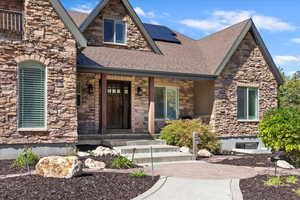 View of front facade featuring stone siding, solar panels, a porch, and roof with shingles