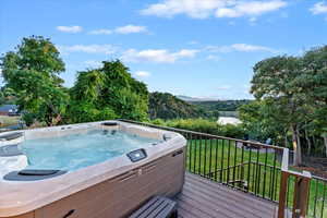 Wooden deck with a wooded view, a hot tub, and a lawn
