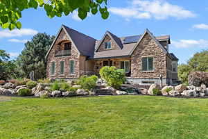 View of front of home featuring stone siding, a front lawn, and roof mounted solar panels