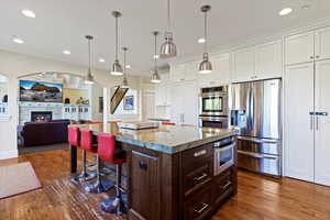 Kitchen featuring dark brown cabinets, appliances with stainless steel finishes, white cabinets, a kitchen breakfast bar, and light stone counters