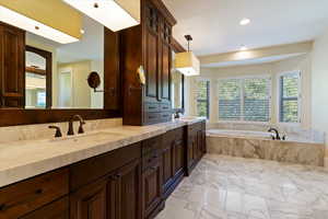 Full bathroom with double vanity, a garden tub, light marble finish flooring, and recessed lighting
