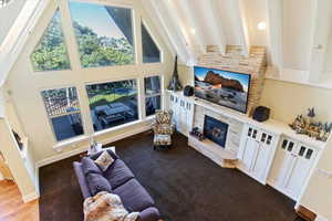 Living area featuring a fireplace, beamed ceiling, high vaulted ceiling, and dark colored carpet