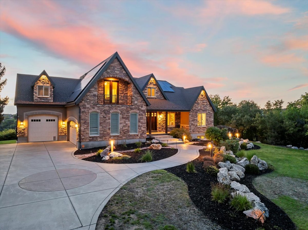 View of front facade with stone siding, curved driveway, a yard, and solar panels