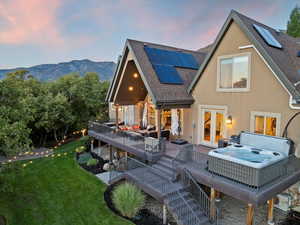 Back of house with a deck with mountain view, a shingled roof, a hot tub, solar panels, and a yard