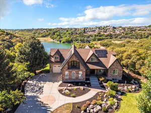 View of front of home featuring stone siding, driveway, covered porch, roof mounted solar panels, and a water view