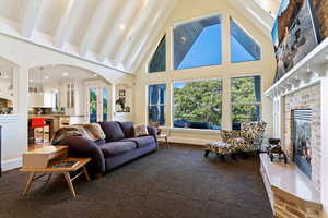 Living area with high vaulted ceiling, a stone fireplace, arched walkways, dark colored carpet, and recessed lighting