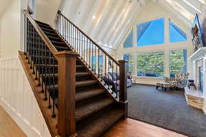 Staircase featuring high vaulted ceiling, wood finished floors, a brick fireplace, and beam ceiling