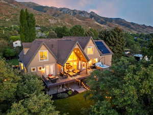 Back of property at dusk with an outdoor living space, a deck with mountain view, a lawn, a hot tub, and stucco siding