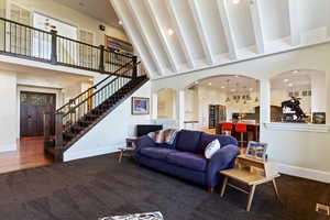 Living area featuring recessed lighting, a towering ceiling, dark colored carpet, stairway, and arched walkways