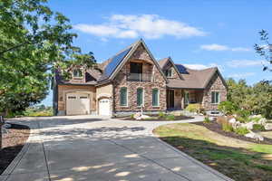 View of front of house featuring stone siding, concrete driveway, roof mounted solar panels, a garage, and a balcony